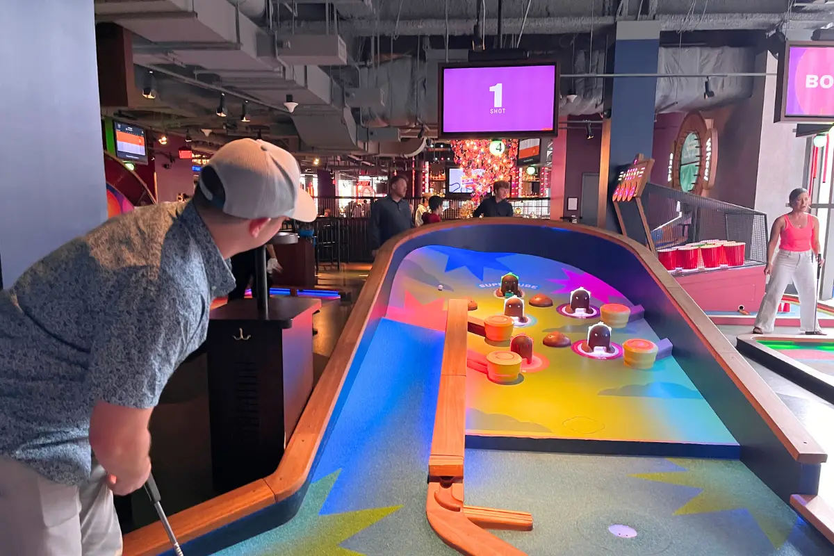 Man about to hit his ball at mini golf, on a pinball themed putt