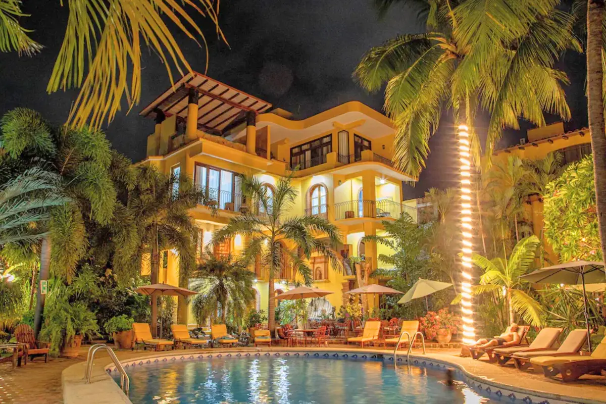 Hotel Suites La Hacienda hotel lit up at night at the pool deck with palm trees overhead which shows how much of a tropical paradise the hotel is