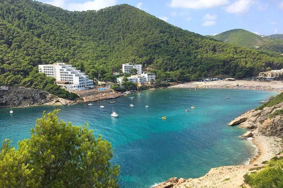 The secluded Cala Llonga beach and mountains, with crystal clear blue water and boats