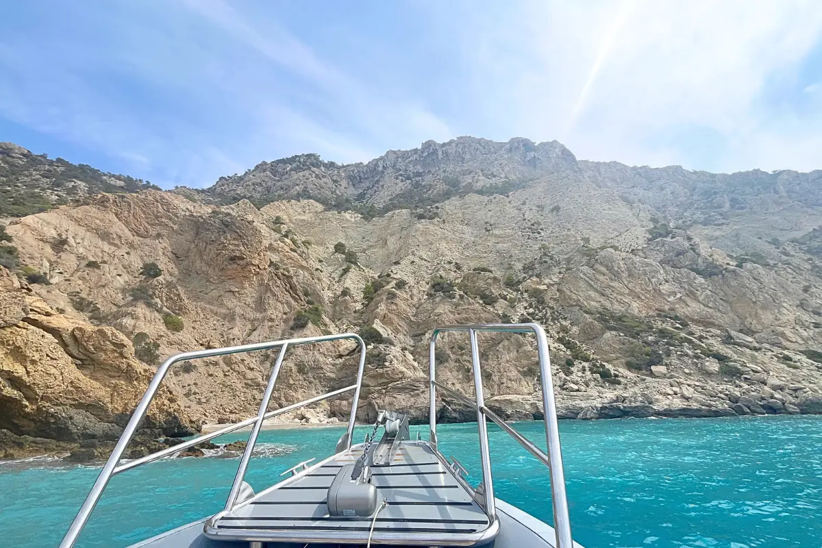 A boat approaching Es Vedra in Ibiza with the sun shining and bright blue water underneath the limestone cliffs