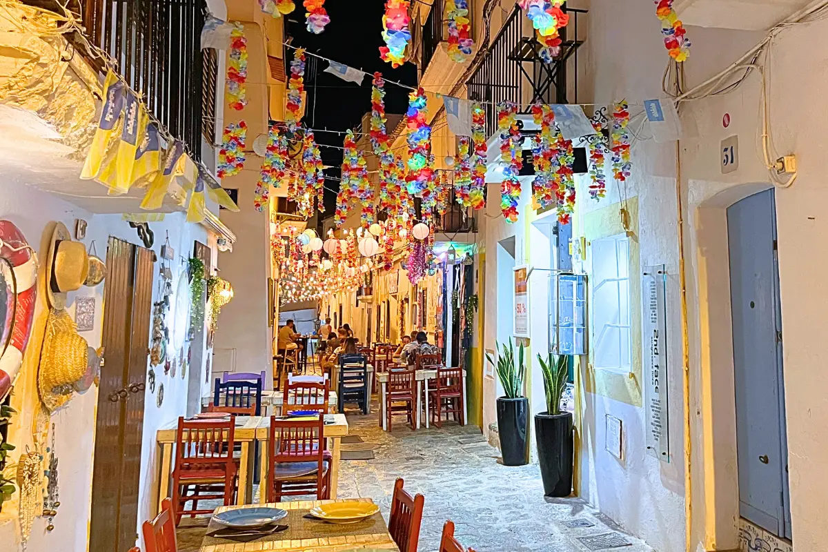 A side street in Ibiza Town at night with rainbow leis hanging down 