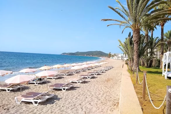 Playa den Bossa in Ibiza, with mountains in the back and beach loungers on a bright sunny day