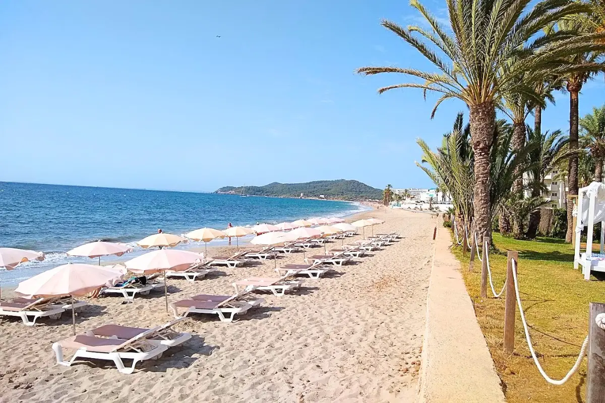 Playa den Bossa in Ibiza, with mountains in the back and beach loungers on a bright sunny day