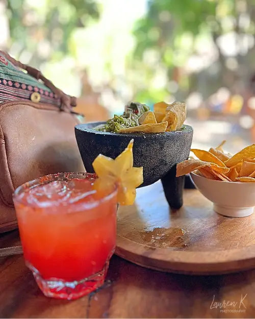 Guacamole and a pretty red cocktail with star fruit in front of a tropical paradise, to show the amazing food and drinks options available at Selina Puerto Escondido