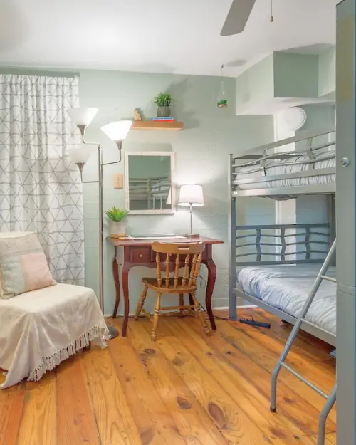 A dorm room with industrial style bunk beds and a nice chair with wood flooring