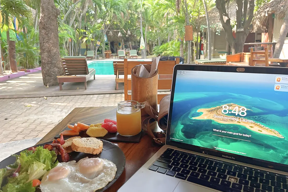 A POV view of a laptop and breakfast entree in front of the pool area at Selina Puerto Escondido, to show one of the many spaces you can work remotely at the hostel