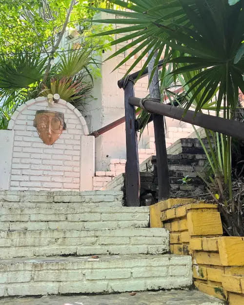 Steep outdoor stone steps with a monkey decoration and lush palm trees and foliage surrounding it 