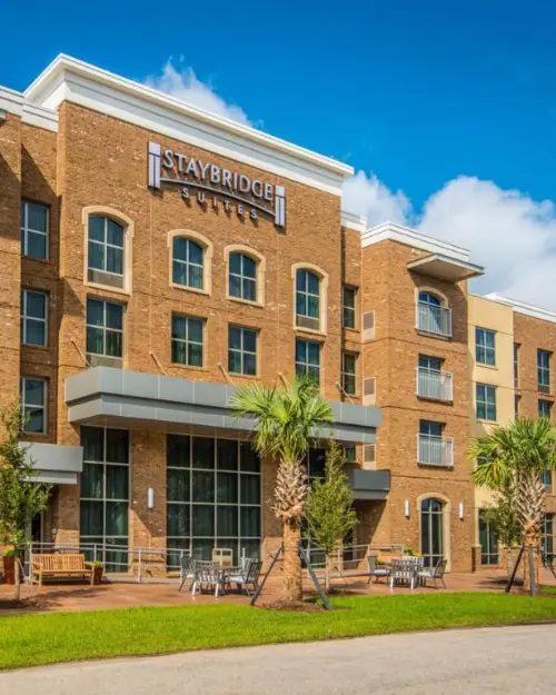 The bright and sunny exterior of the Staybridge Suites with plants and palm trees under a bright blue sky