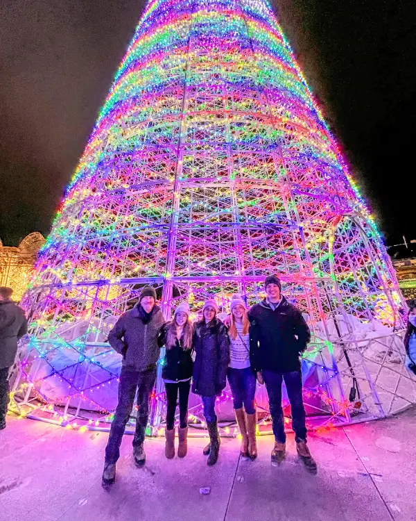 A group of 5 standing in front of a giant lit up Christmas tree at Enchant at National's Park