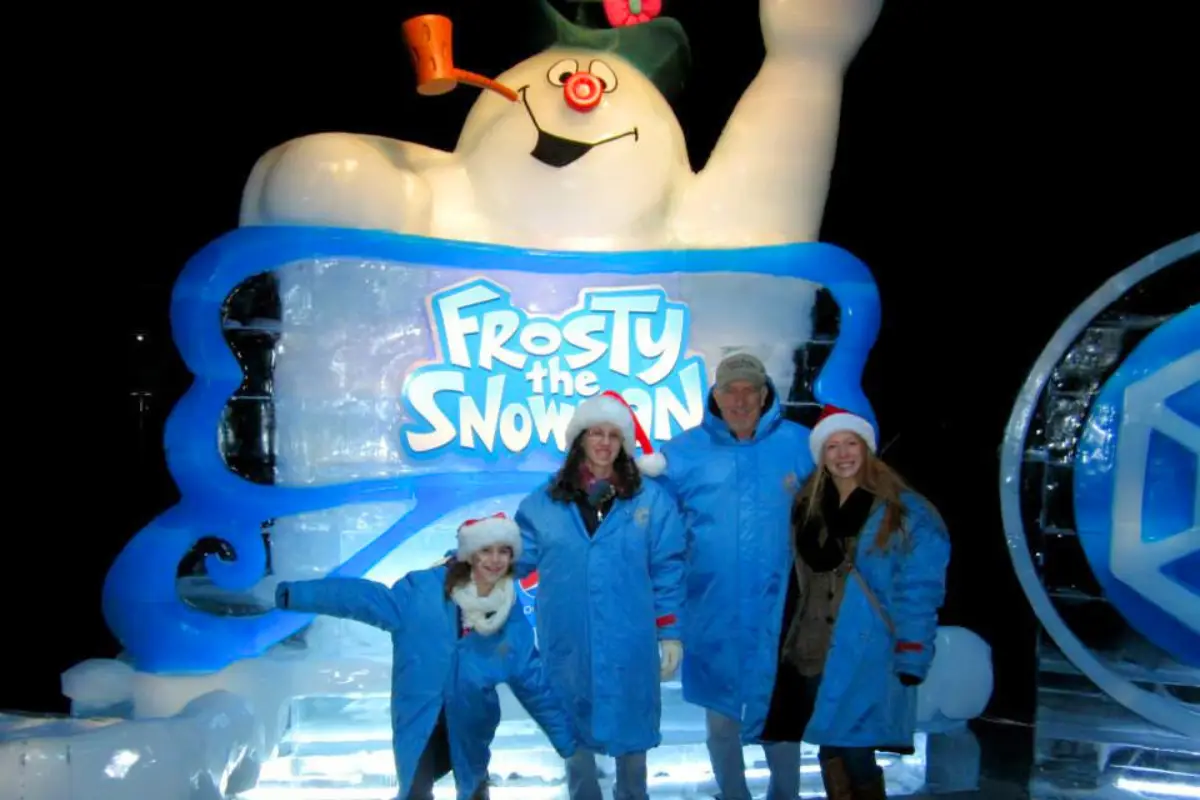 A family of 4 in front of the big Frosty the Snowman sign at ICE! with giant parkas and santa hats