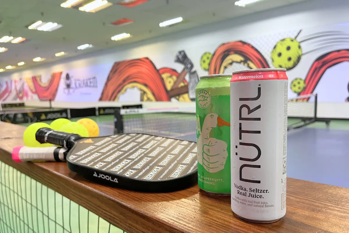 Pickleball paddles and two drinks in front of a pickleball court