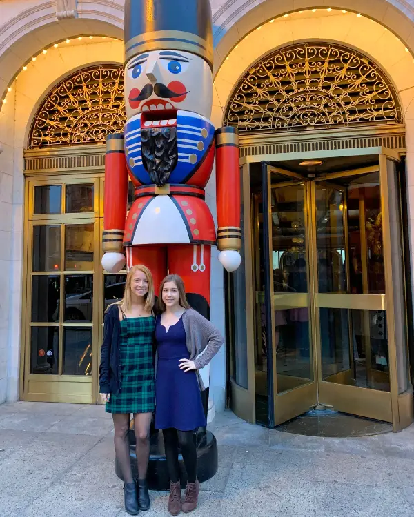 Two sisters standing dressed up during Christmas time in front of a giant nutcracker which is at Old Ebbit Grill in Washington DC