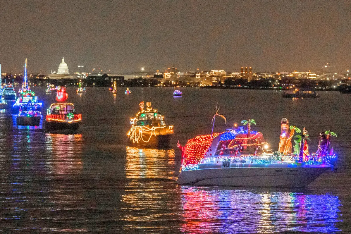 A bunch of boats lit up with holiday lights in a line coming down the Potomac for the District Holiday Boat Parade, which is one of the best Downtown Washington DC Christmas events and things to do