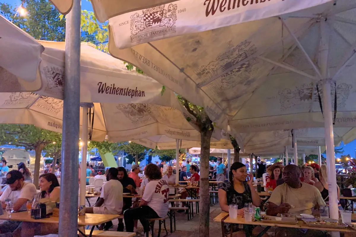 A crowded outdoor space at Dacha Beer Garden in Navy Yard with everyone sitting at tables under umbrellas at night time