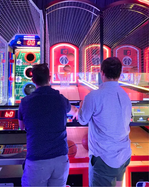 Two men playing basketball at Dave and Busters, both playing on one machine