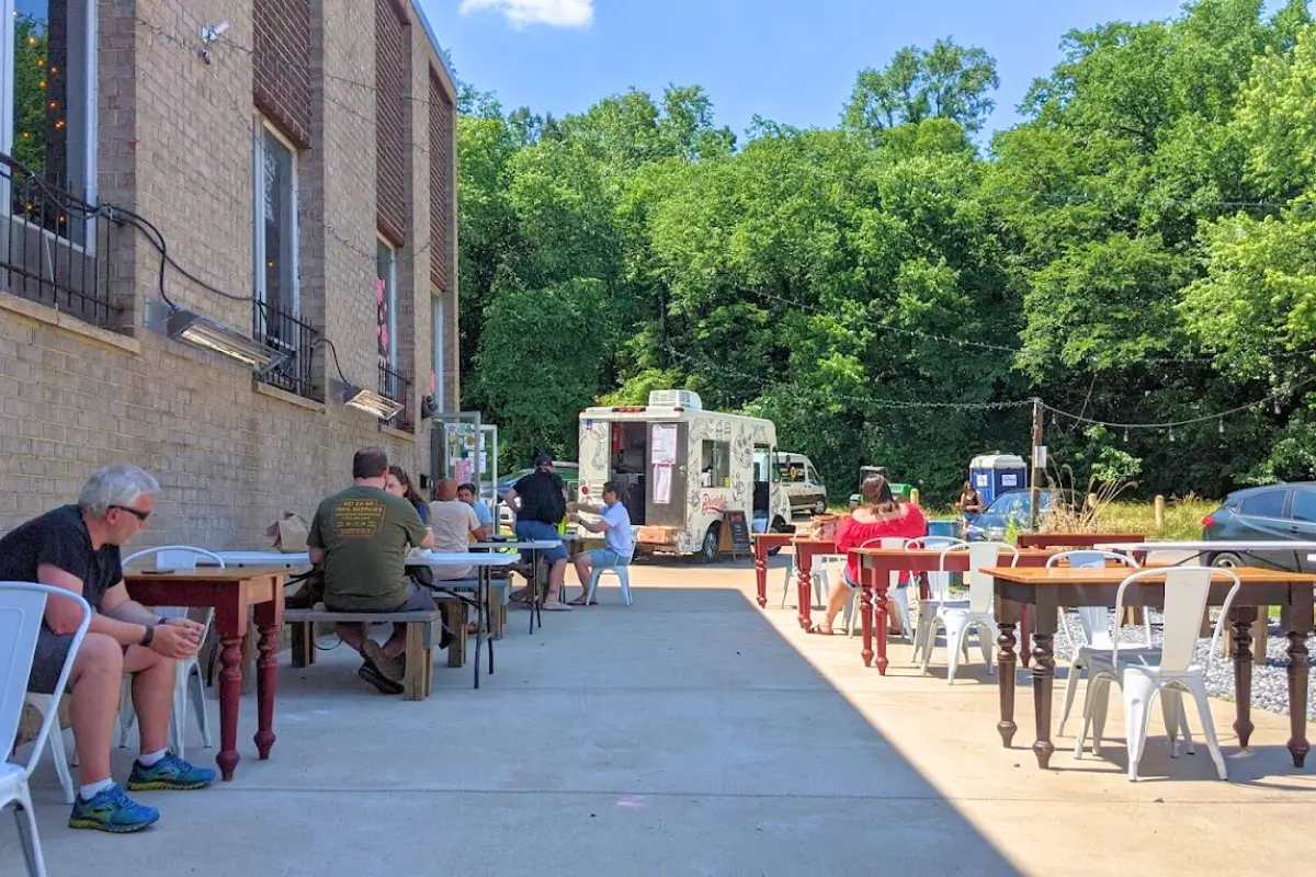 Outdoor tables and food truck on a sunny day with people hanging out at Hellbender Brewery DC