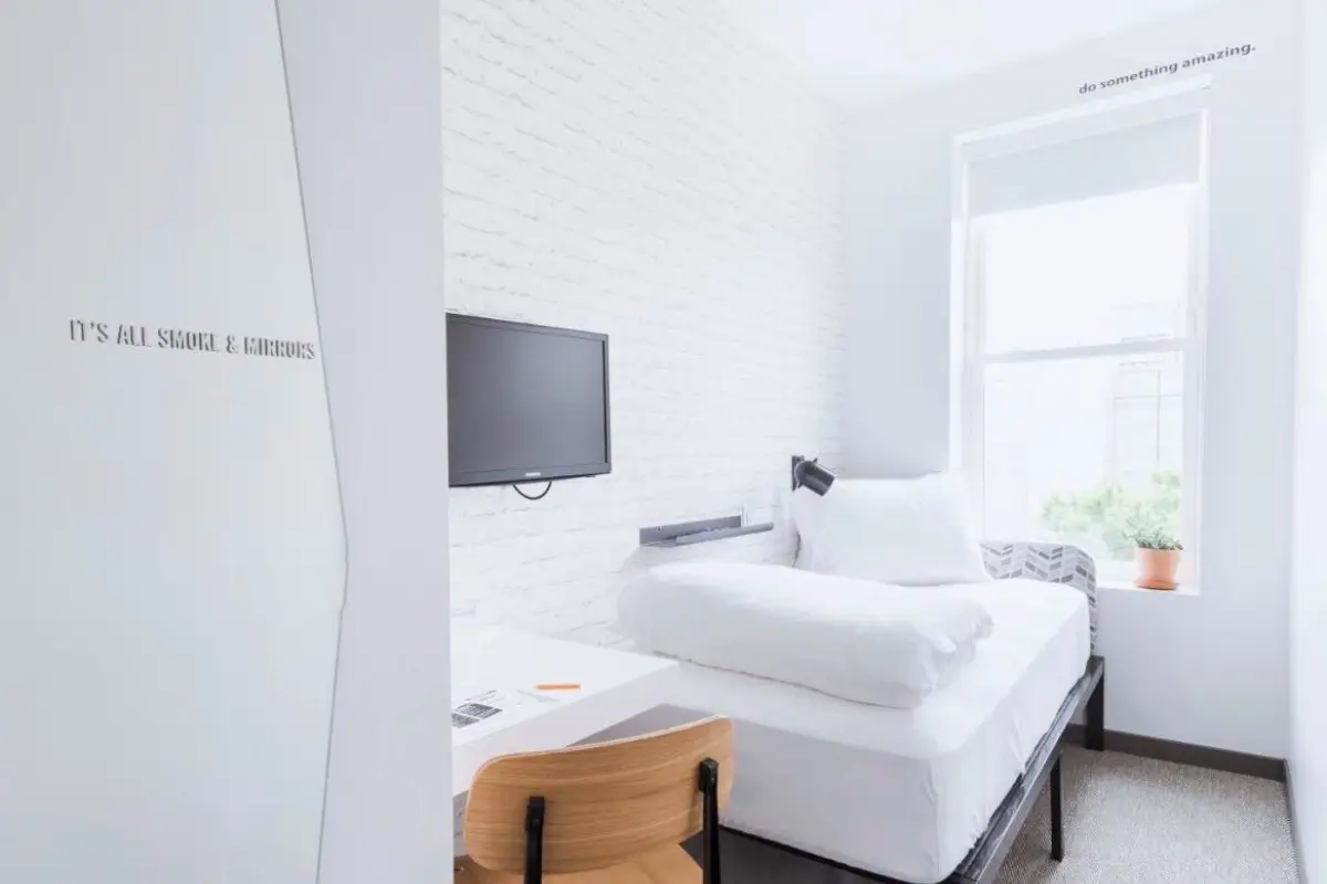 Small room at the Hive hotel in Washington DC which has room for a small sing, single bed, a tiny desk and a TV, to help example what is a micro hotel as an example