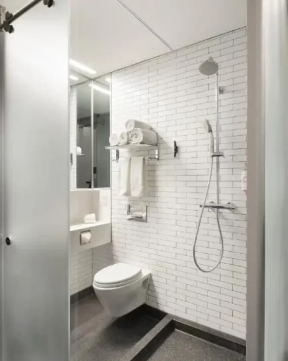 Small bathroom which has the toilet coming out of the wall in the same room as the shower head and sink, which shows how small the typical micro hotel en suite bathroom would be 