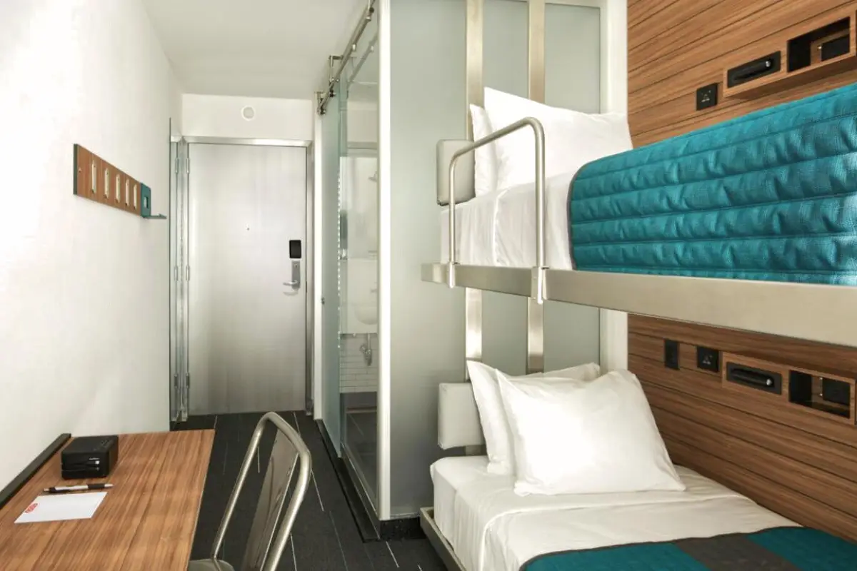 A bunk bed room at the Pod Hotel Times Square micro hotel, which shows a small room with an en suite bathroom and small desk, to help define what is a micro hotel