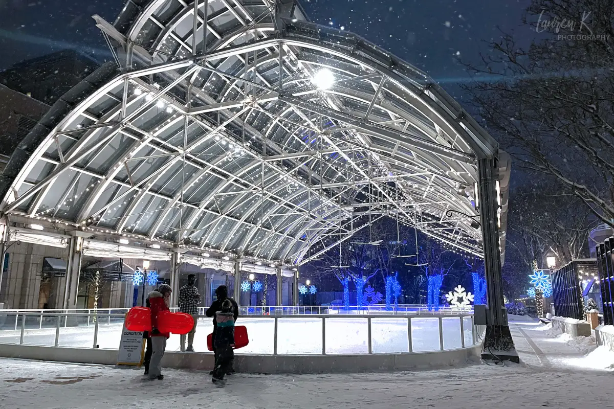 A family with sleds in hand talking to the attendant at the Reston Town Center ice skating rink during a snowy night