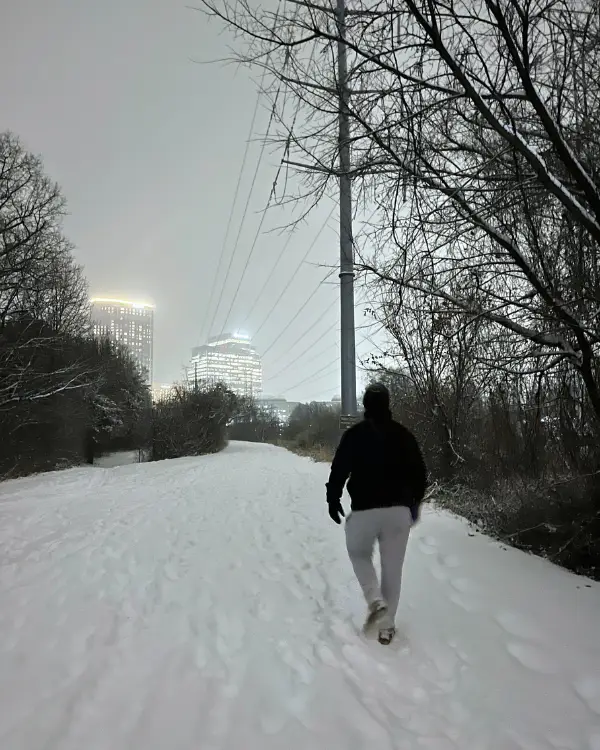 Man walking down the W&OD trail with lit up buildings in the background and snow on the ground