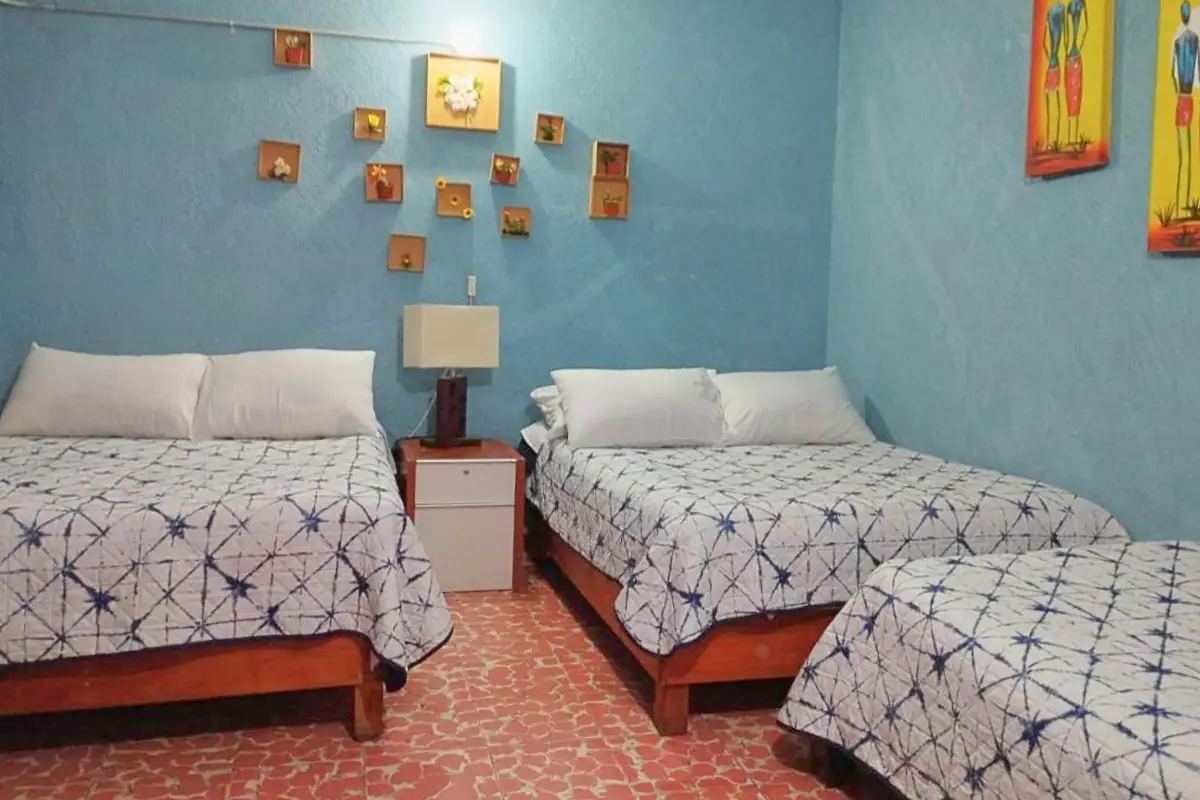 A room with two double beds and a twin bed with blue walls and basic furnishings, at the Alo Mexico hotel 