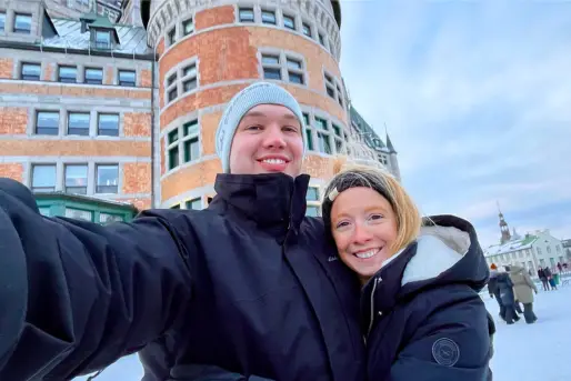 Greg holding out the camera to take a selfie of us while we're bundled up in the snow in front of the Fairmont Le Château Frontenac