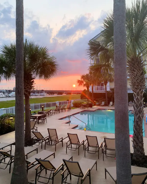 Sunset over the peaceful Courtyard Charleston Waterfront pool deck with palm trees and lounge chairs all around