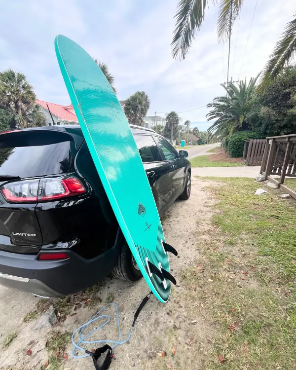 A surf board leaned up against a car parked at Folly Beach