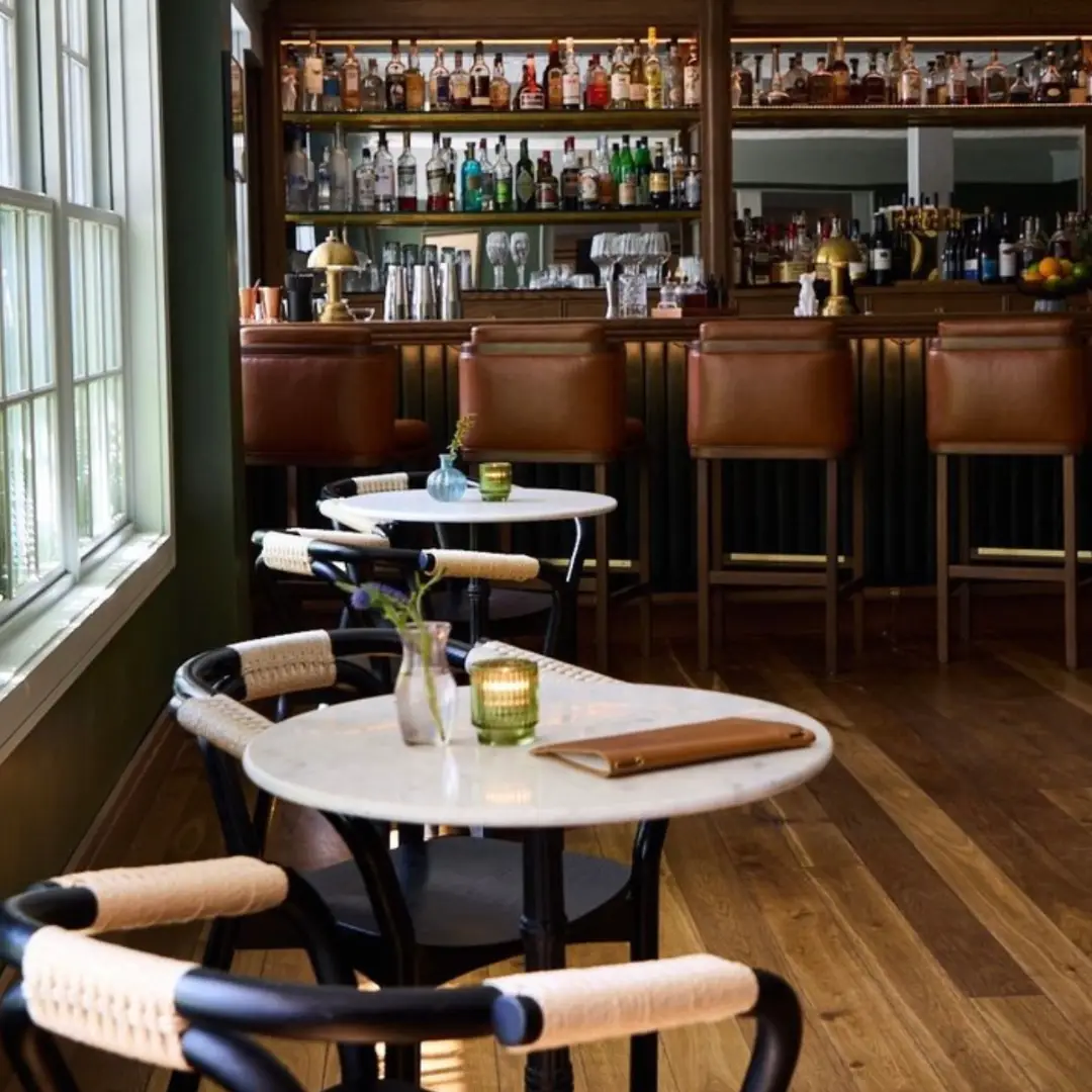 Two person tables and a bar with bar seats in a sunny space