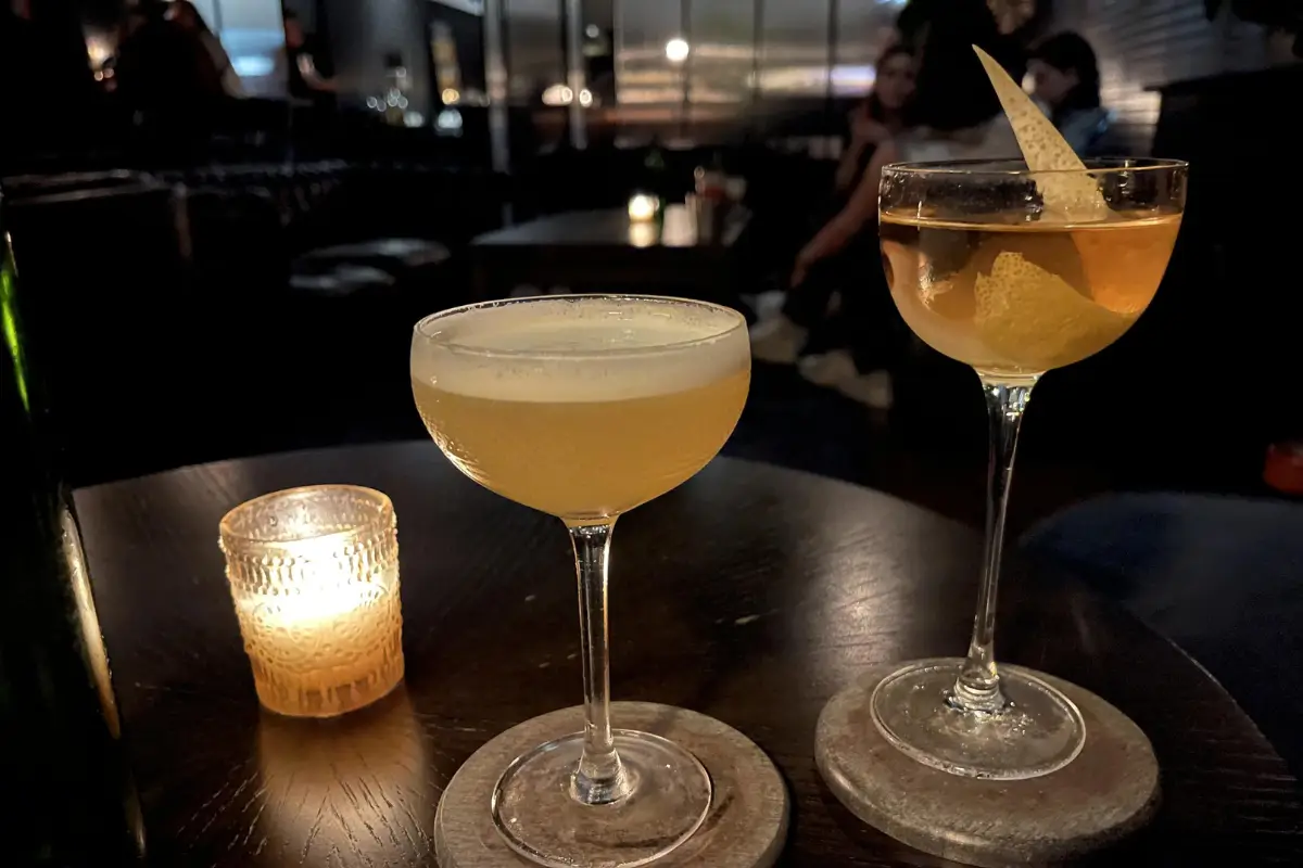 Two craft cocktails in elegant glasses on a dark table with a candle lit