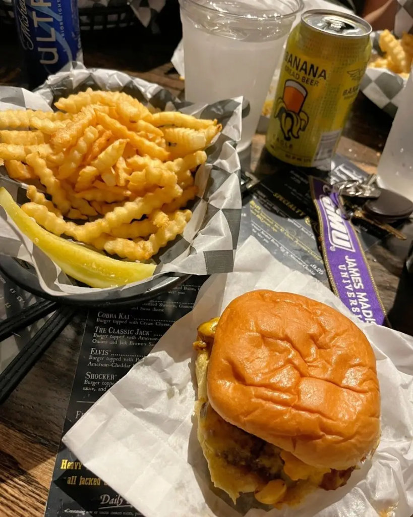 A large basket of crinkle fries and a cheesy burger in a dimly lit restaurant
