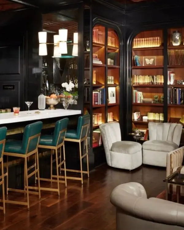 The speakeasy Charleston SC at the Spectator hotel, with tall bookshelves, a bar with art deco furniture and cozy lounge chairs